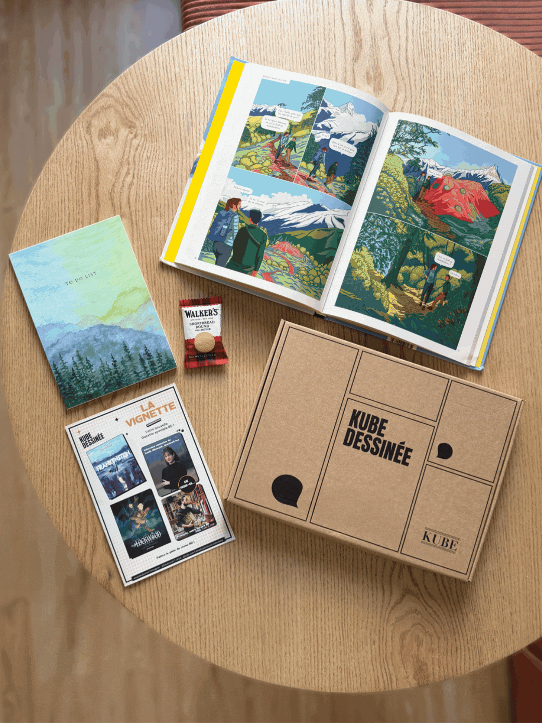 Box BD Kube Dessinée ouverte sur une table en bois, abonnement BD adulte par libraire indépendant.